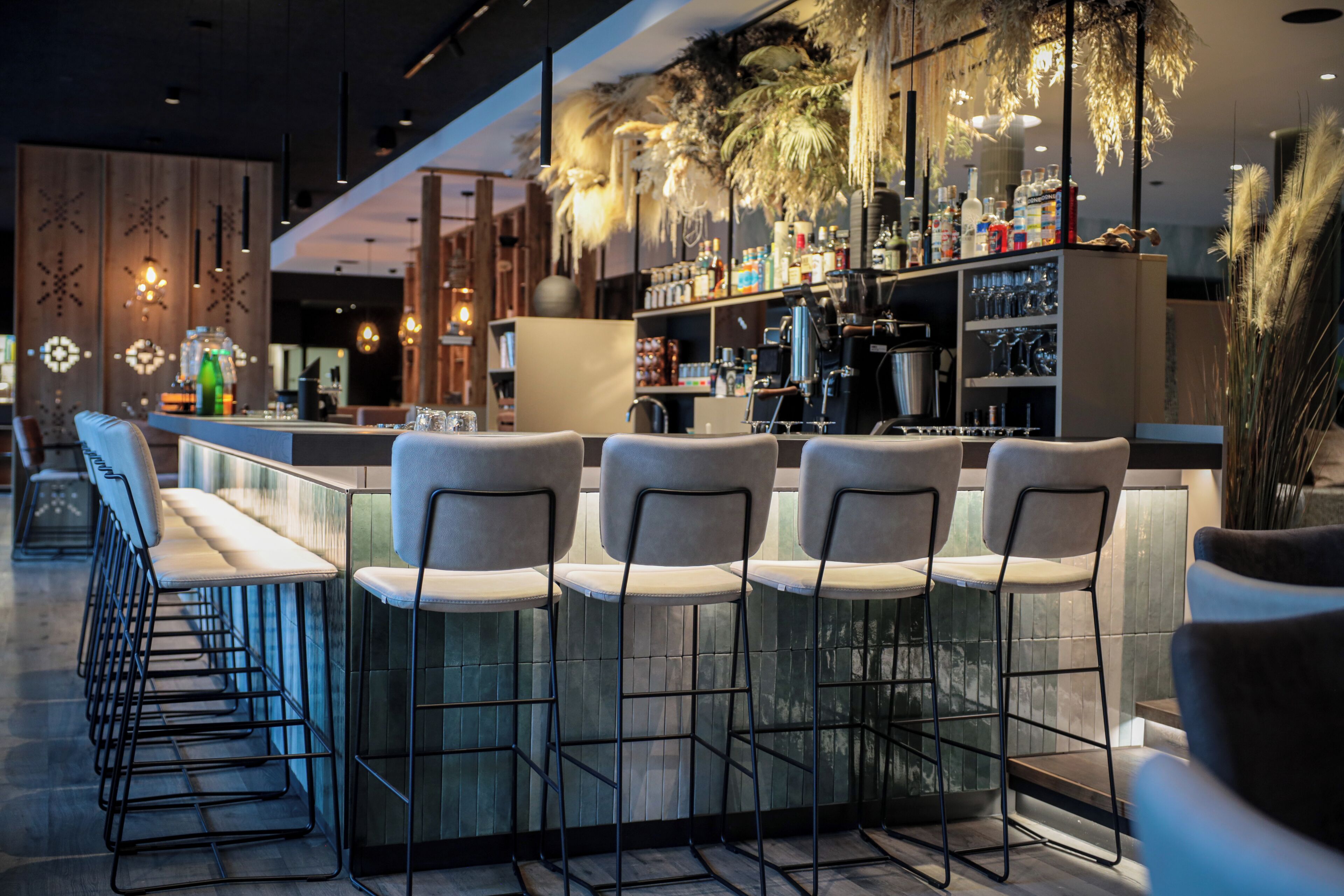 A bar area with high stools and a bar counter, equipped with a coffee machine and various bottles.