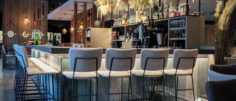 A bar area with high stools and a bar counter, equipped with a coffee machine and various bottles.