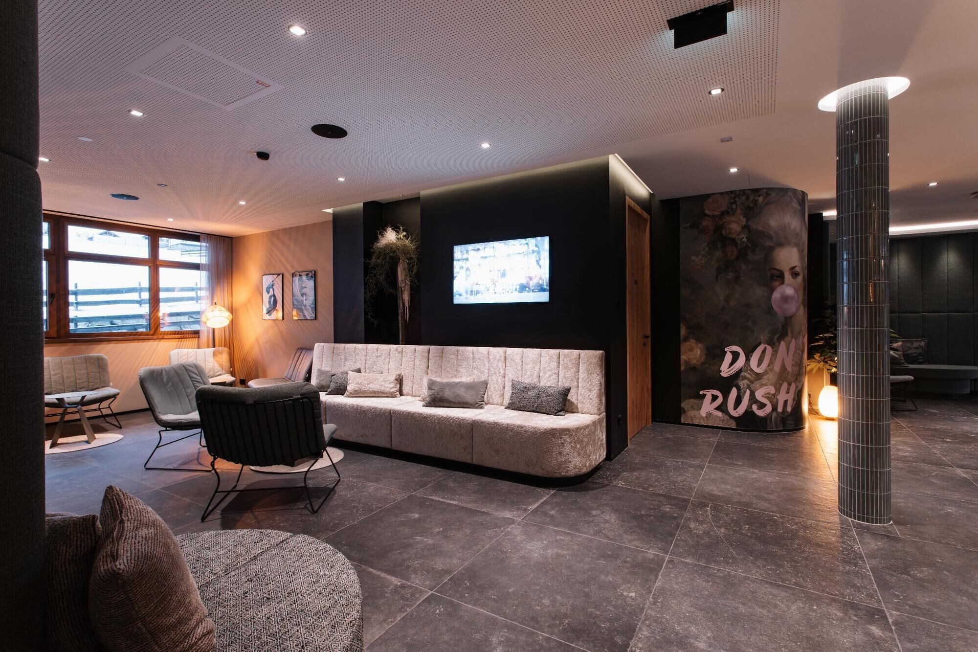 Eine moderne Lobby mit einer gebogenen Couch, einem großen Bildschirm und einem Schild mit der Aufschrift 'DON'T RUSH'.