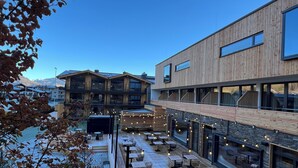 Il s’agit d’un bâtiment moderne doté d’une façade en bois et de grandes fenêtres. Une cour intérieure offre des espaces de détente en plein air et une vue sur les montagnes en arrière-plan.