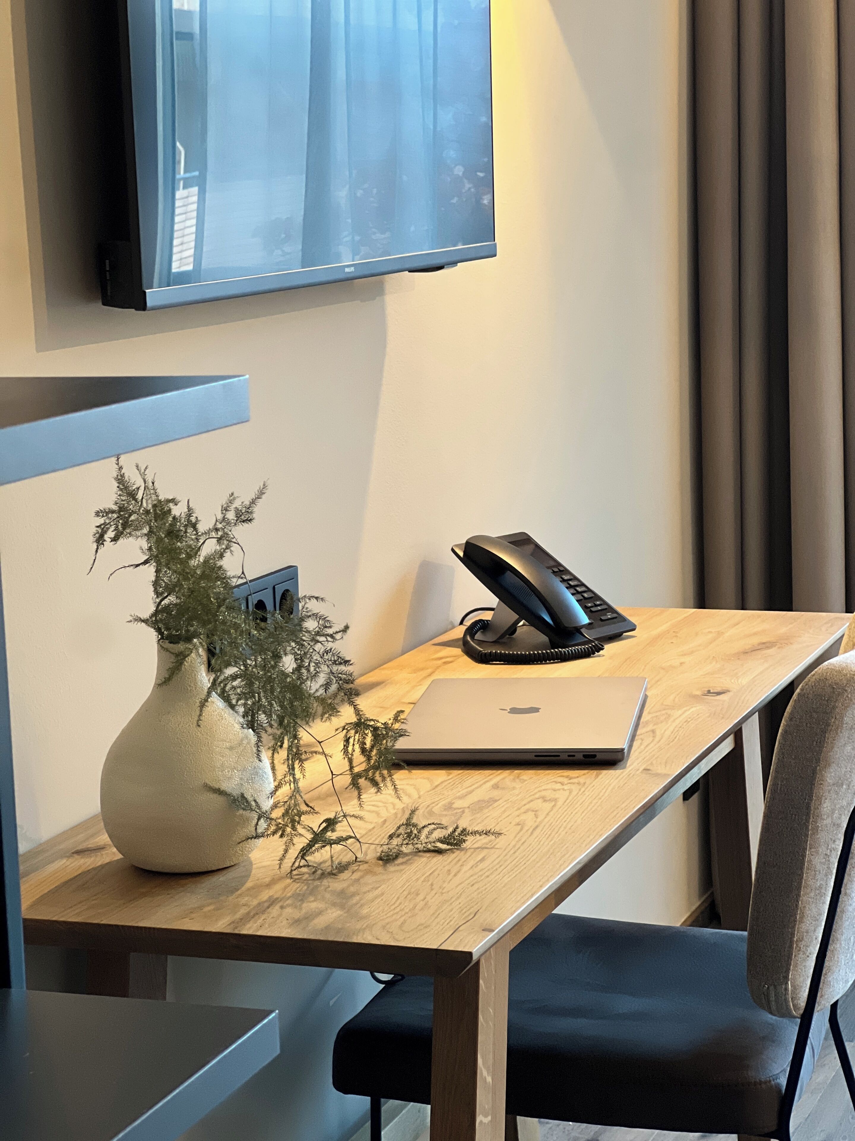Een modern bureau met een laptop, een telefoon en een decoratieve plant.