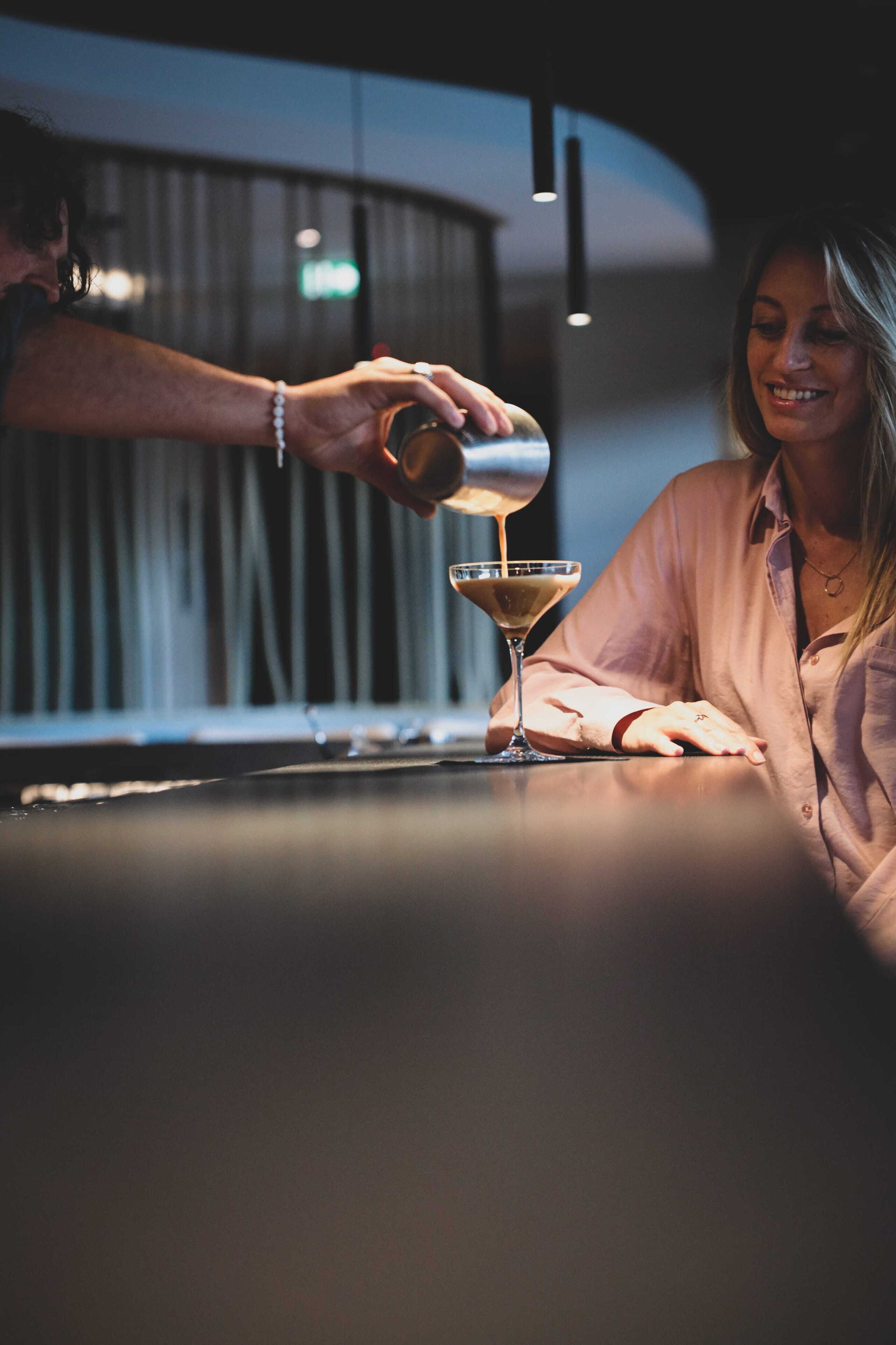 Une personne verse une boisson dans un verre à martini sur le comptoir d’un bar.