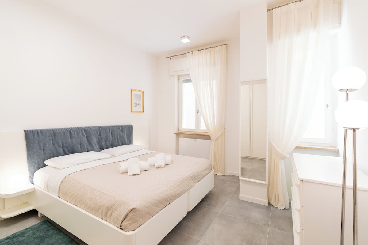 A modern bedroom with a bed, bedside tables, a window with curtains, and a mirror.
