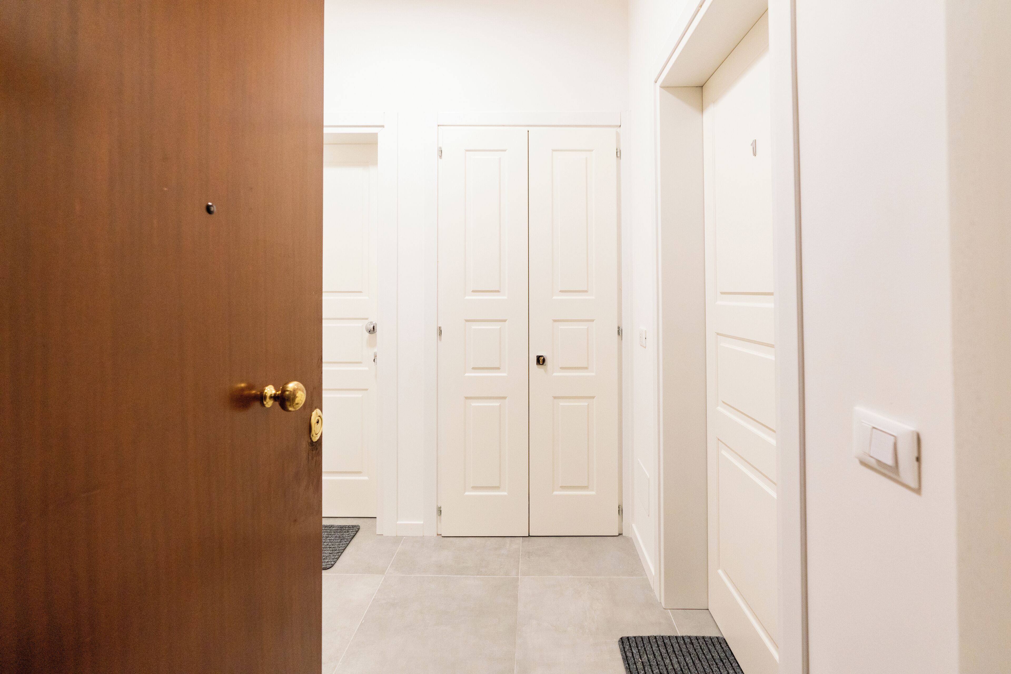 Un pasillo con una puerta de madera a la izquierda, una puerta blanca en el centro y otra puerta blanca a la derecha.