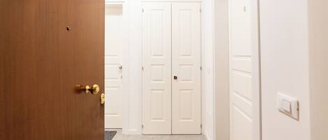 Un pasillo con una puerta de madera a la izquierda, una puerta blanca en el centro y otra puerta blanca a la derecha.