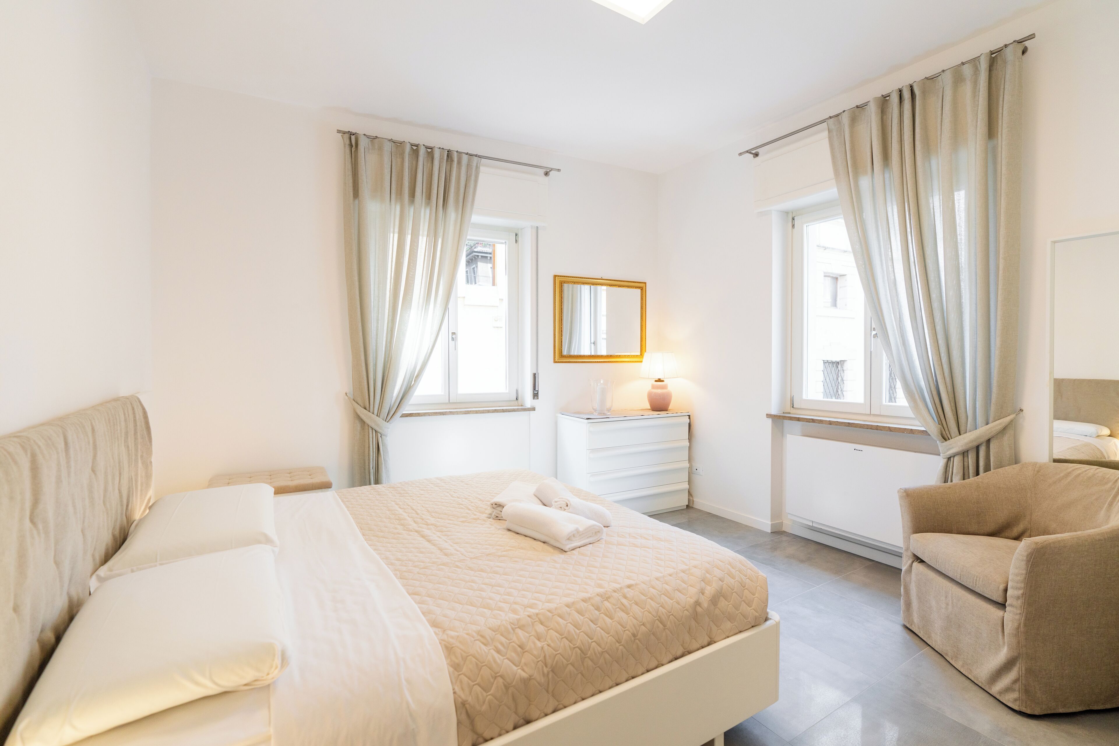 A bedroom with a bed, a chair, a nightstand, and a window with curtains.