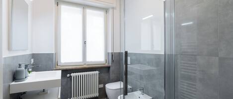 Et moderne badeværelse med glasvæg omkring brusenichen, en hvid vask og toilet.