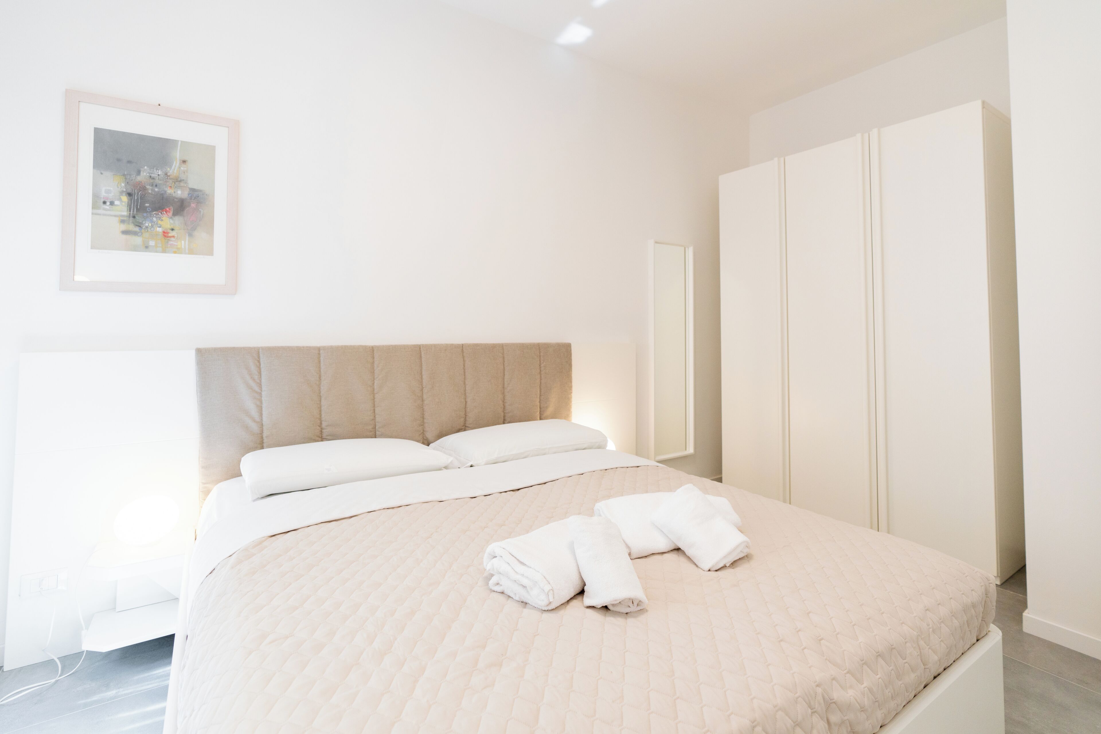 Una cama bien hecha con un cubrecolchón acolchado y dos toallas enrolladas encima.