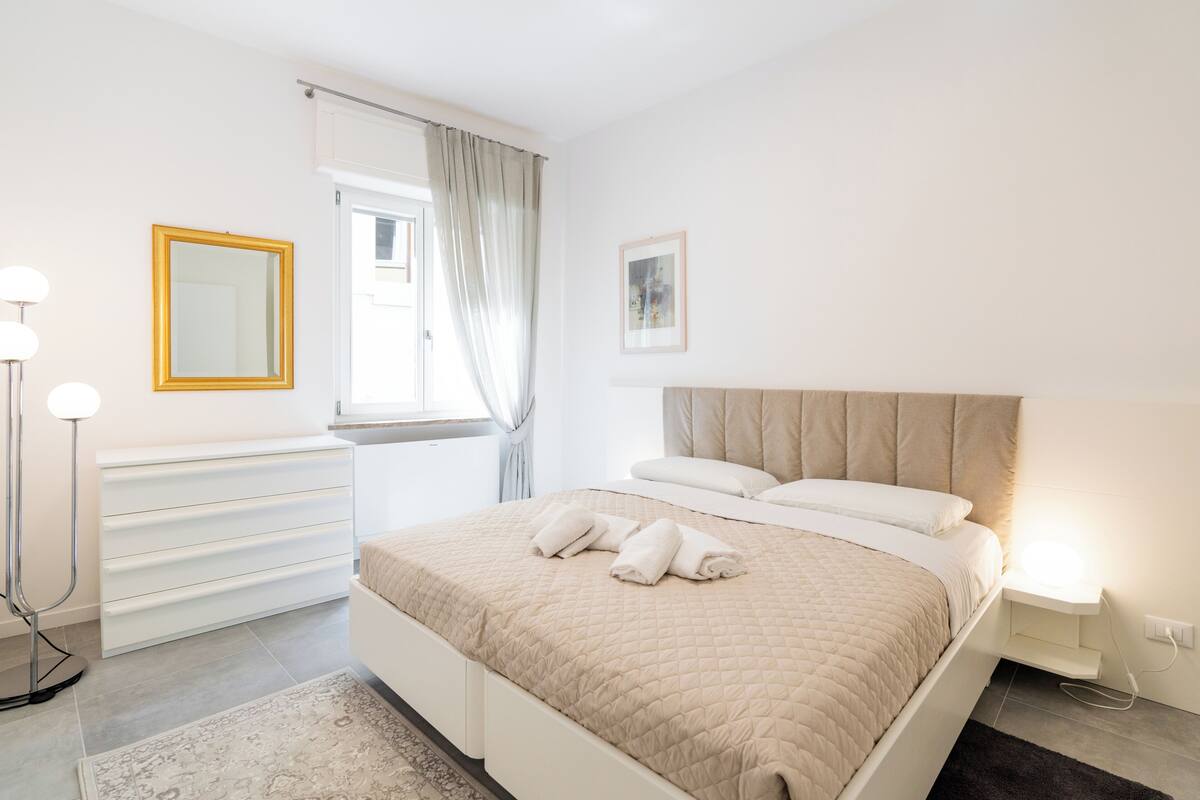 A bedroom with a bed, bedside table, lamp, and a window with curtains.
