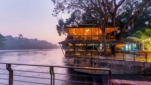A riverside restaurant with outdoor seating, a view of the river, and a covered area with tables and chairs. - Silverbill Resorts  (Joida)