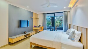 A modern hotel room with a large bed, a flat-screen TV, a desk with a chair, and a balcony with a view of trees. - Silverbill Resorts  (Joida)