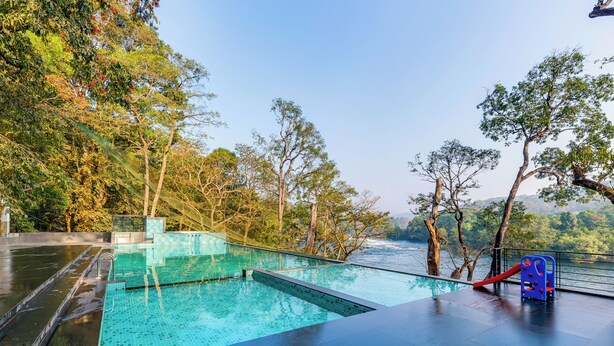 An outdoor swimming pool with a slide, surrounded by trees and a view of a river. - Silverbill Resorts  (Joida)
