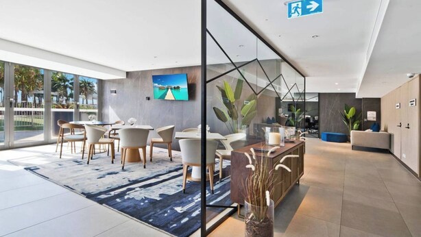 En moderne hotellobby med en stor glasvæg, en reception og et siddeområde med borde og stole.