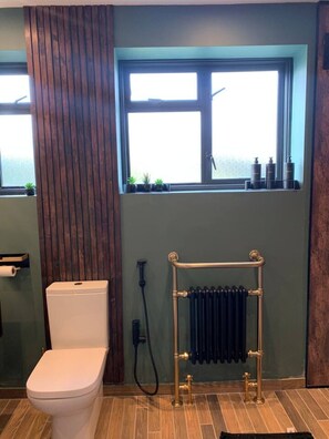 Ein Badezimmer mit Toilette, Heizkörper und zwei Fenstern mit Pflanzen.