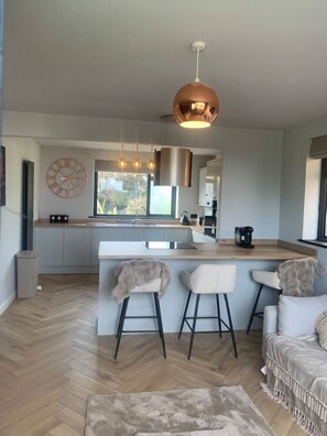 A modern kitchen with a central island, pendant lighting, and a large window. - Luxury Apartment- Beach 10mins (Thorpe Bay)