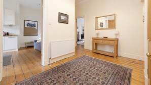 A hallway with a wooden floor, a patterned rug, a wooden console table with a mirror, and a framed picture on the wall.