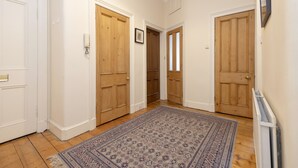 A hallway with three wooden doors, a patterned rug, and a radiator on the wall.
