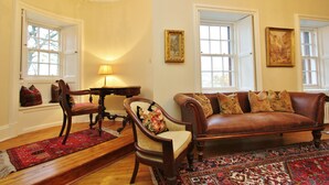 A traditional living room with a brown leather sofa, a wooden chair, a red patterned rug, and a chandelier. - Gorgeous 3-Bedroom Apt Next to Castle & Royal Mile (Edinburgh)