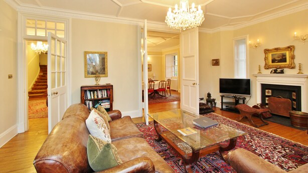A spacious living room with a leather sofa, a glass coffee table, a chandelier, a fireplace, and a television. - Gorgeous 3-Bedroom Apt Next to Castle & Royal Mile (Edinburgh)