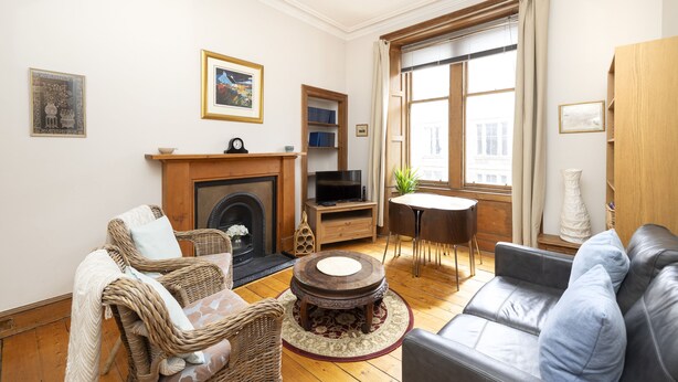 A living room with a fireplace, a television, a sofa, a dining table, and a window with curtains.