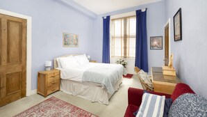 A bedroom with a bed, bedside table, nightstand, dresser, and a desk with a chair.