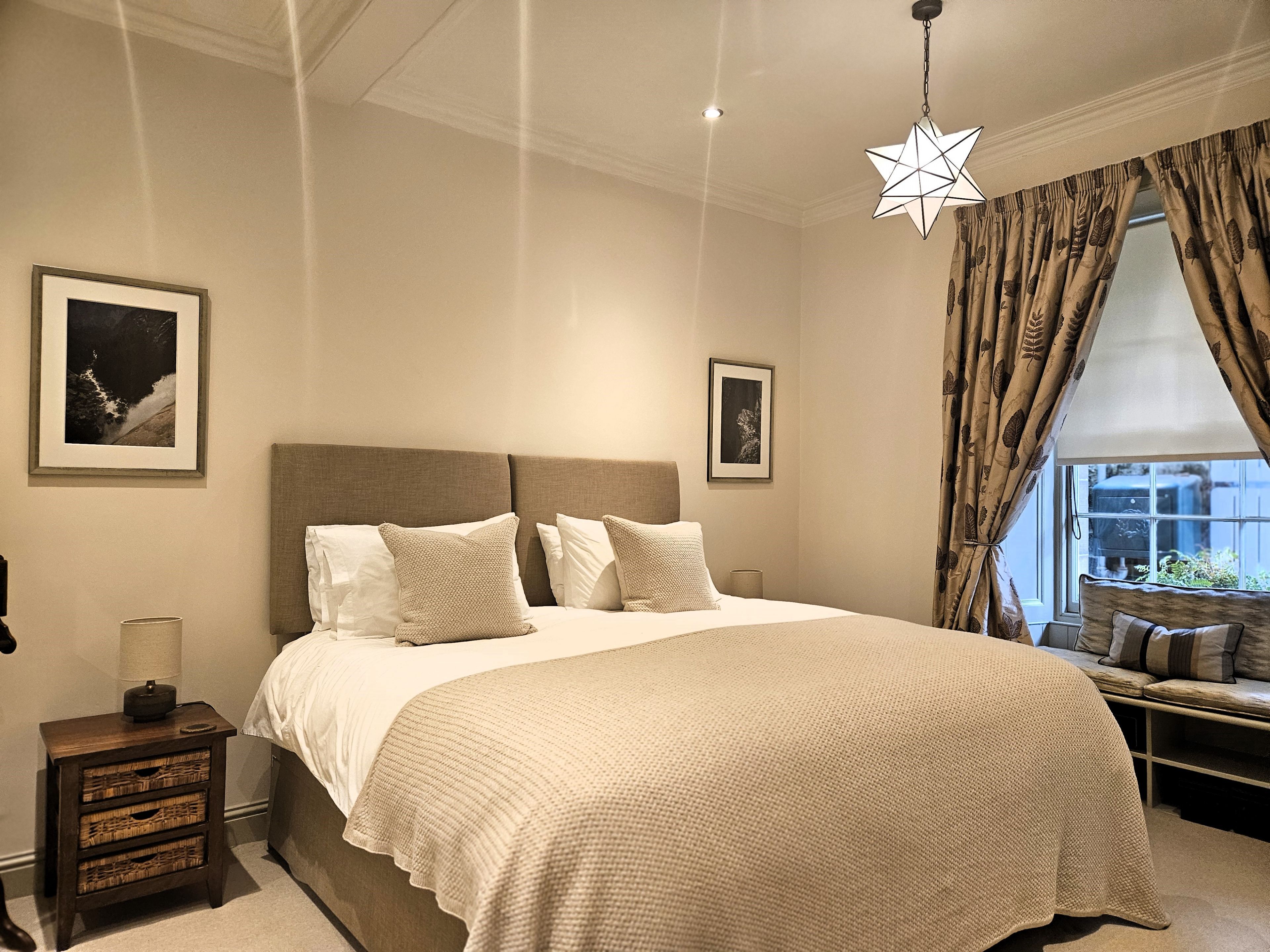A bedroom with a large bed, a nightstand with a lamp, and two framed pictures on the wall.