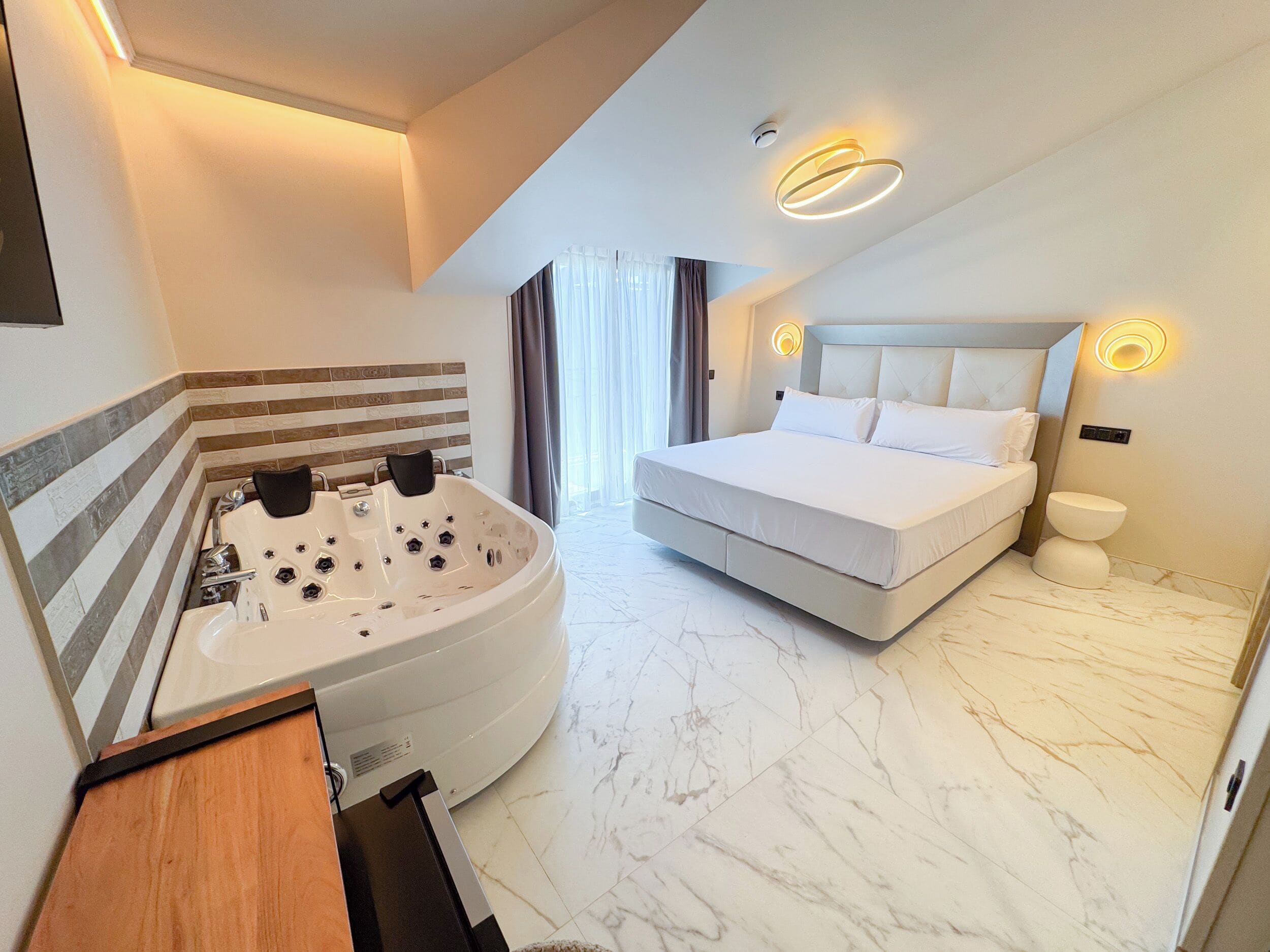Une chambre d’hôtel moderne dotée d’un grand lit, d’une salle de bain séparée avec un jacuzzi et d’un sol en marbre.
