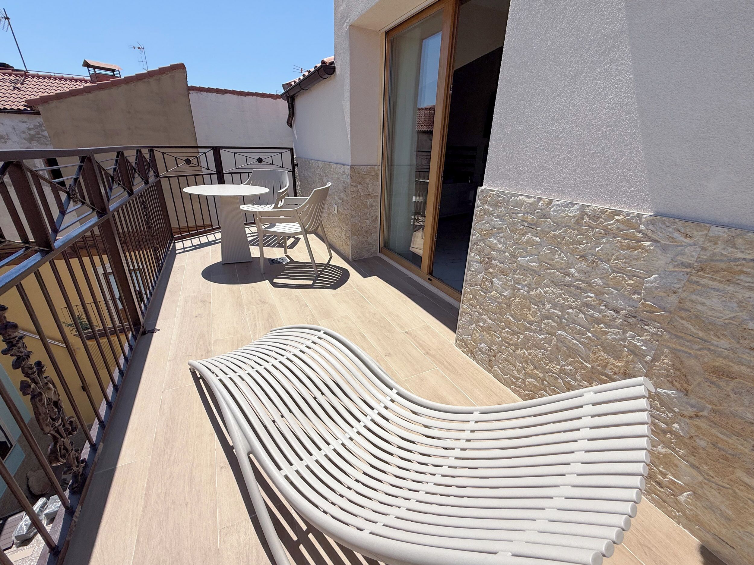 A balcony with a table and chairs, a white chair, and a stone wall.
