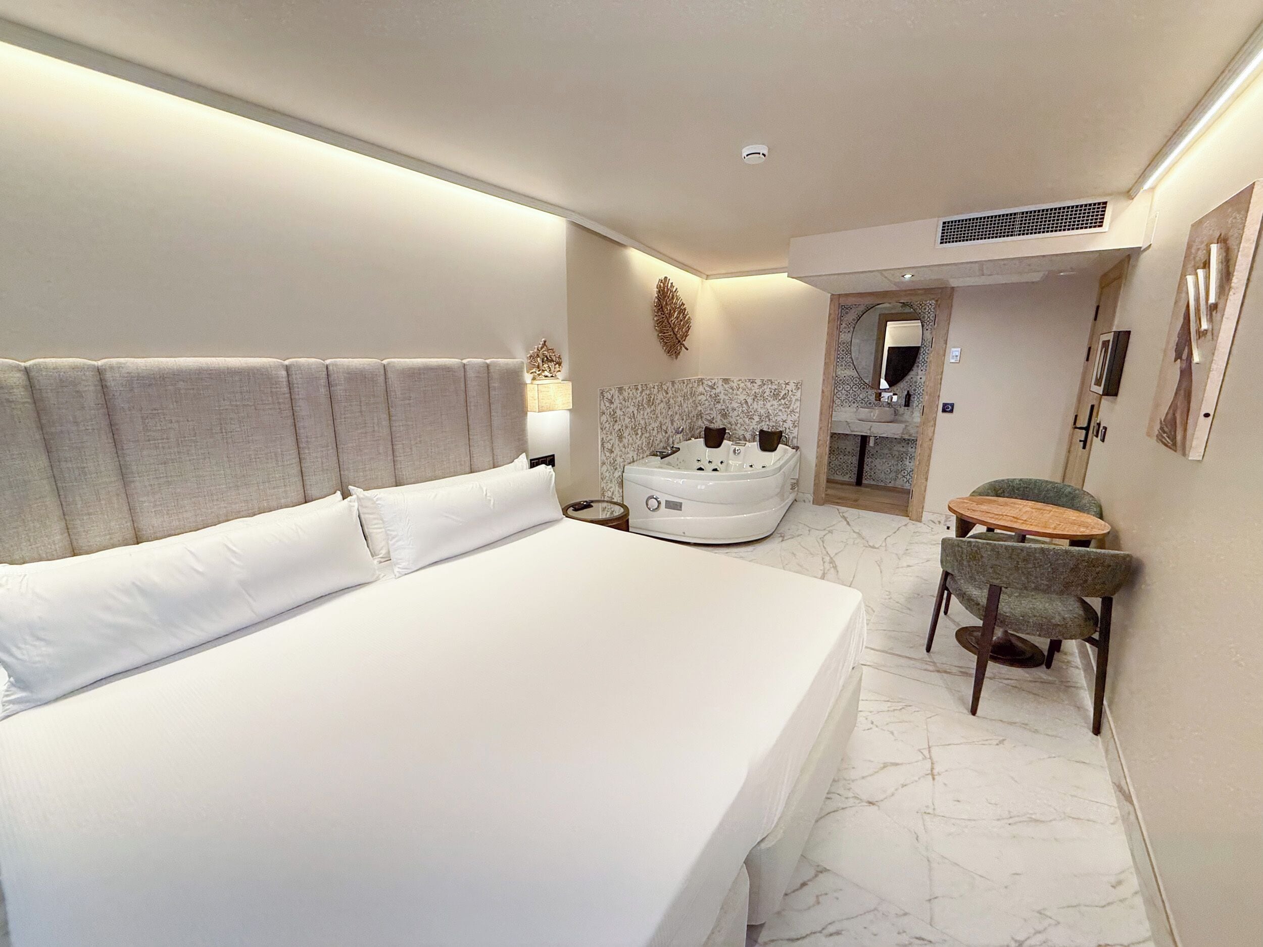 Ein Hotelzimmer mit einem großen Bett, einem eigenen Badezimmer mit Badewanne und einem kleinen Tisch mit Stühlen.