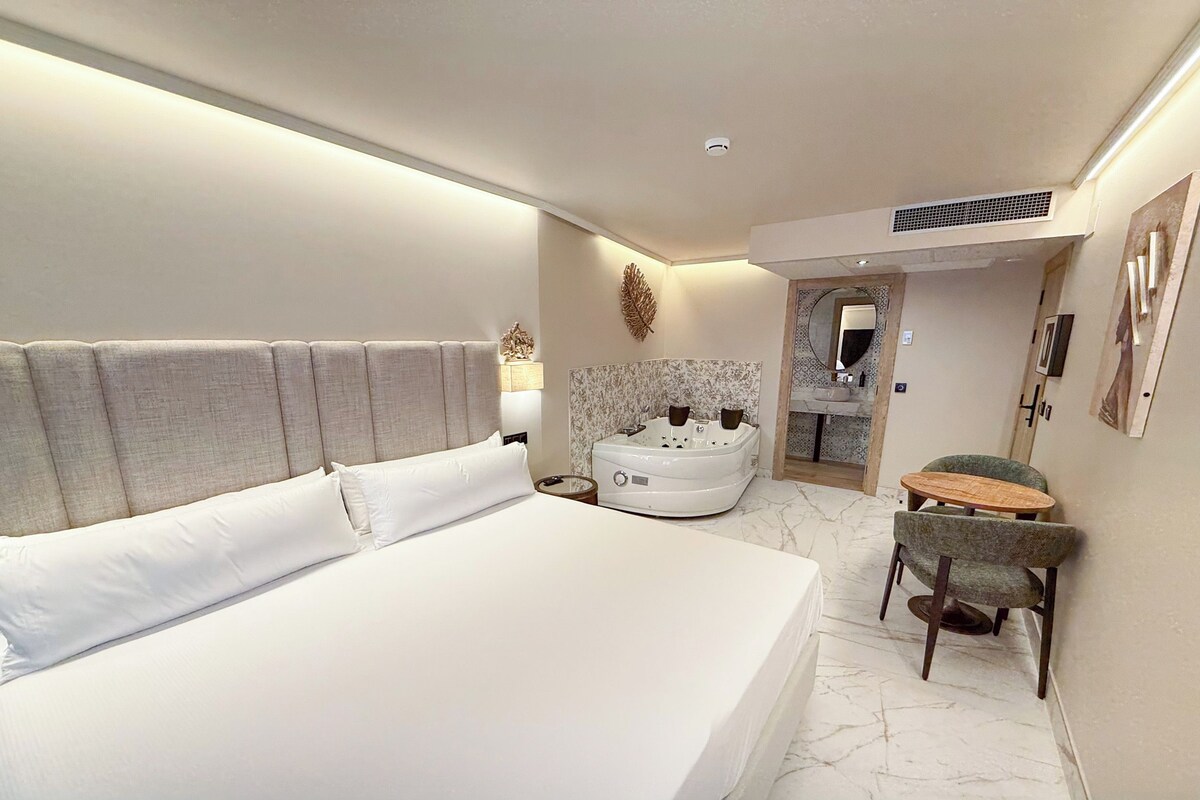 Habitación de hotel con una cama grande, baño independiente con bañera y una pequeña mesa con sillas.