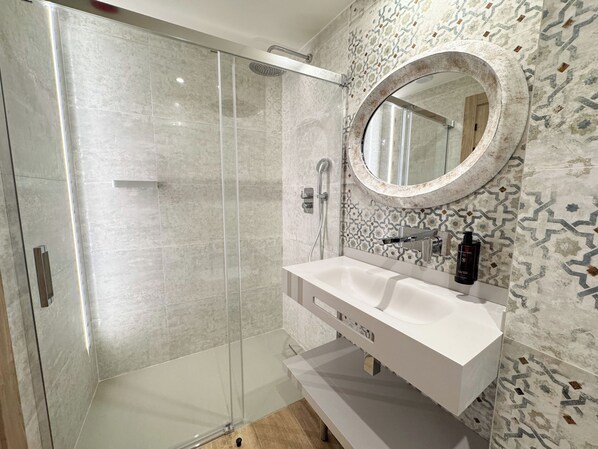 Un baño moderno con ducha envuelta en cristal, tocador blanco y azulejos estampados.