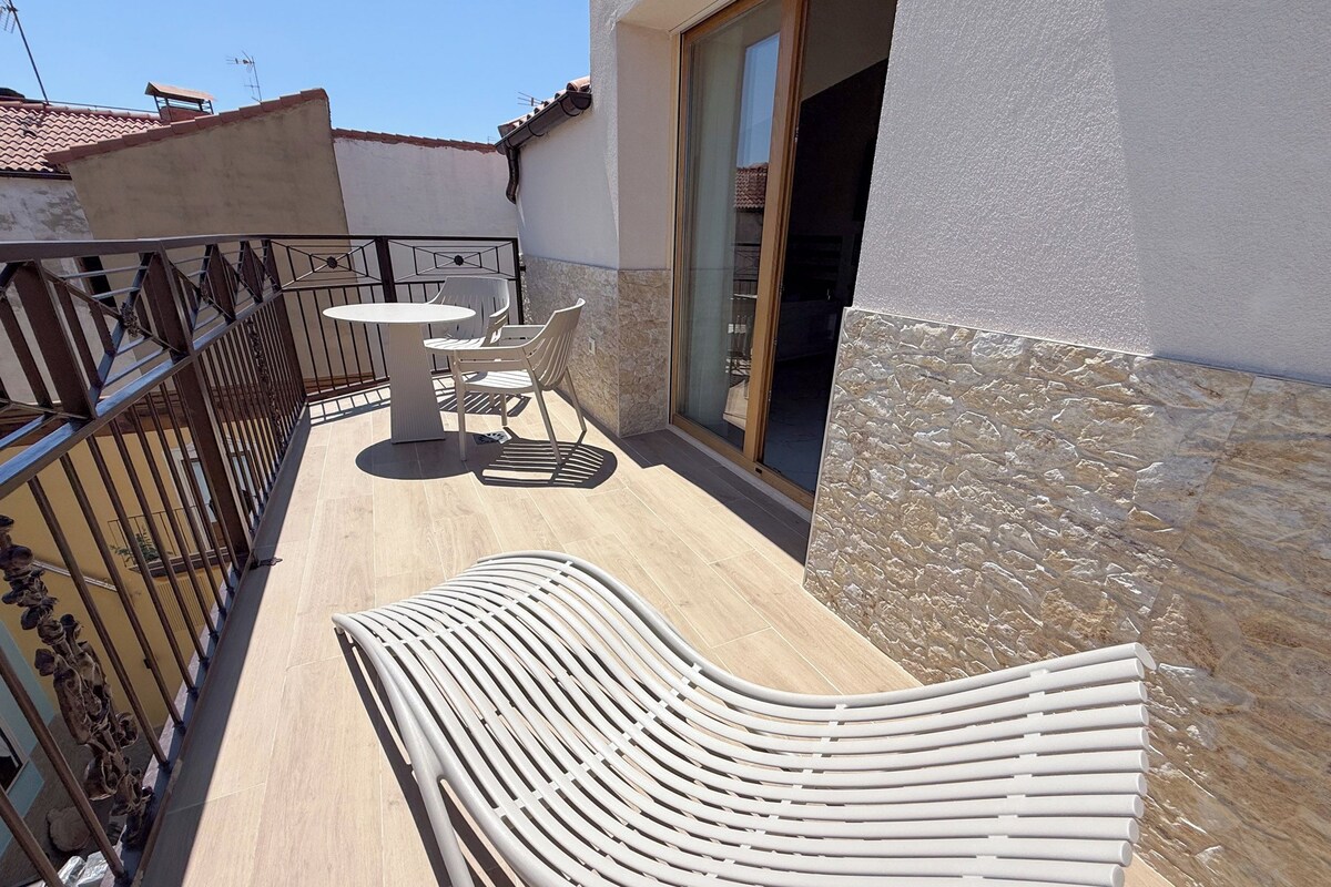 Un balcón con una mesa y sillas, una silla blanca y un muro de piedra.