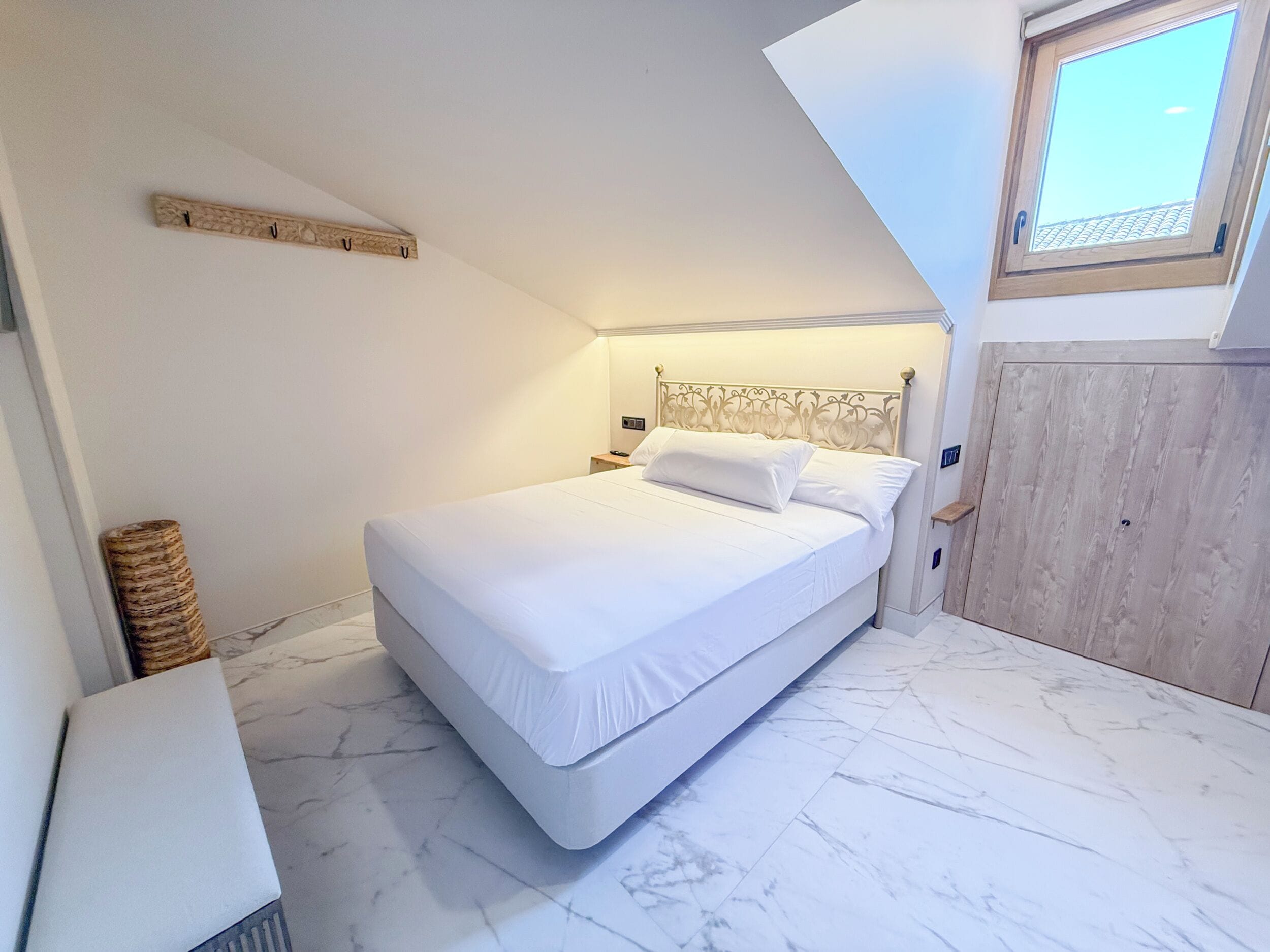 A bedroom with a bed, a nightstand, a wooden headboard, a window, and a wardrobe.