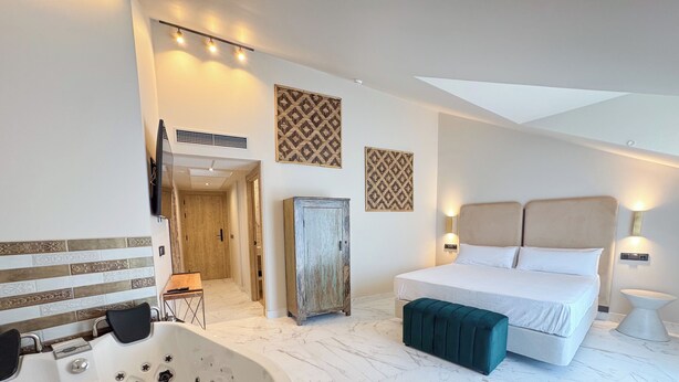 A hotel room with a large bed, a sitting area with a chair, a wooden cabinet, a large bathtub, and decorative wall art. - Akla Hotel El Burgo de Osma (El Burgo de Osma)