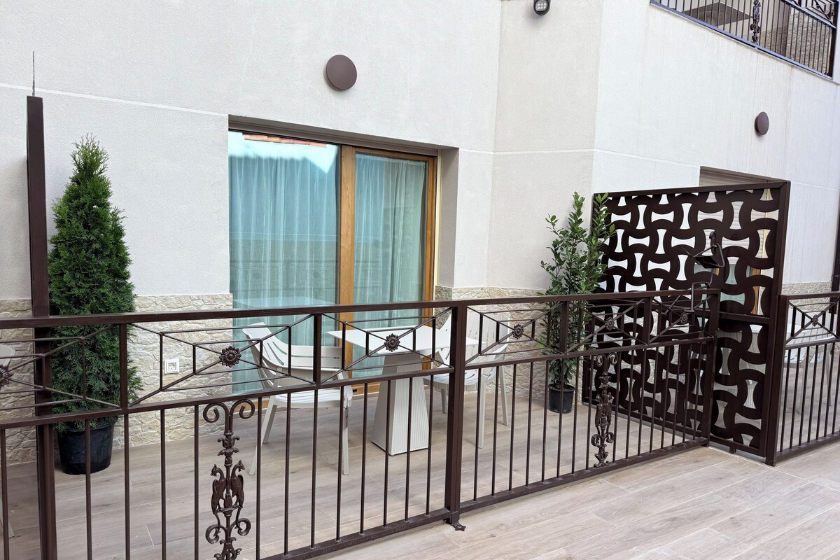 Un balcón con baranda de metal, una planta en maceta y vista a un edificio con ventana y cortinas.