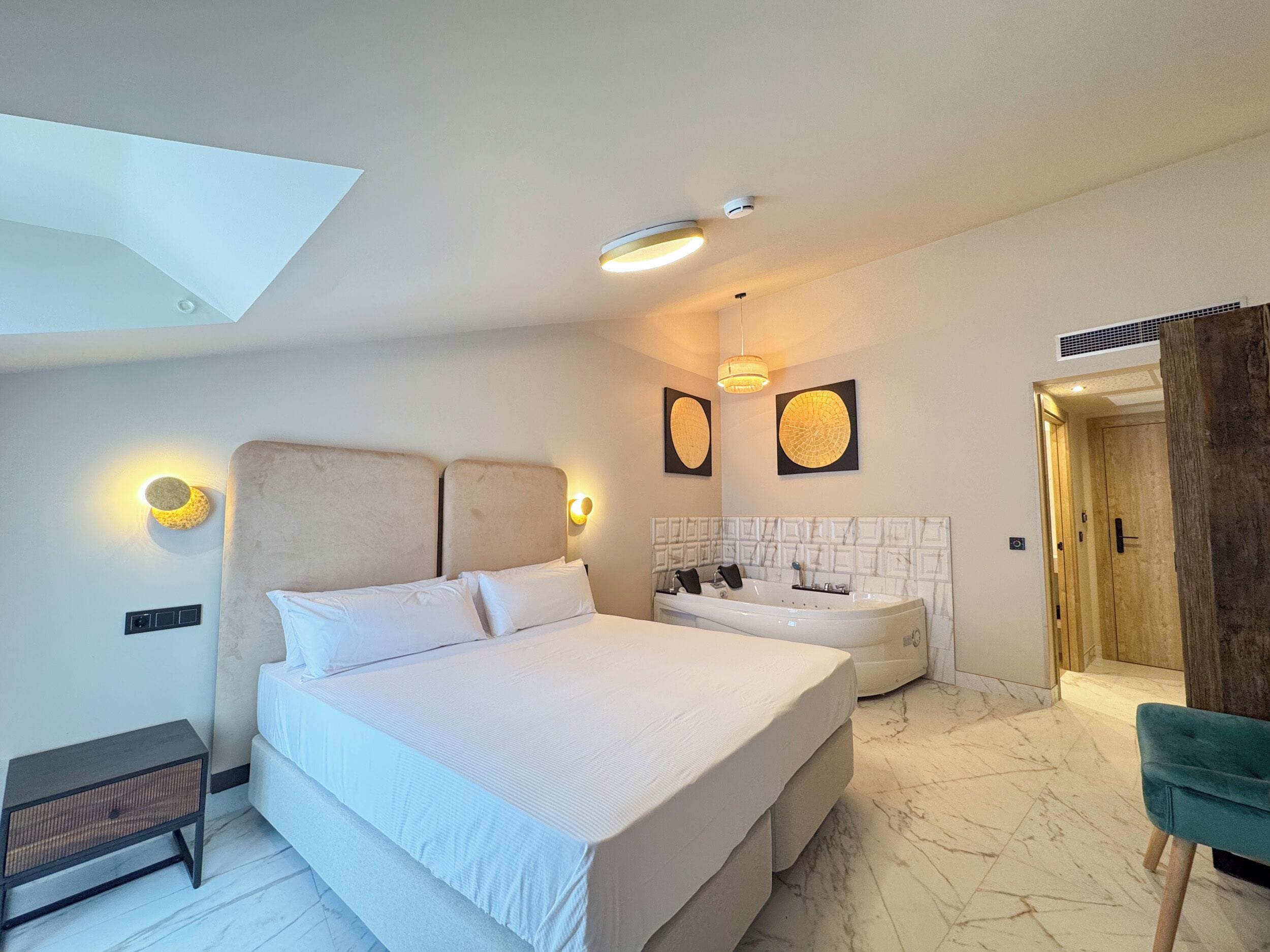 A modern bedroom with a large bed, a built-in bathtub, a vanity, and a wooden door.
