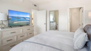 A hotel room with a large bed, a television on a dresser, a mirror, and a door leading to a bathroom. - Beachfront 2BR/2BA condo with pool, Wi-Fi, and ocean views. (Marco Island)