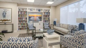 A modern living room with a bookshelf, a sofa, a coffee table, and a TV. - Beachfront 2BR/2BA condo with pool, Wi-Fi, and ocean views. (Marco Island)