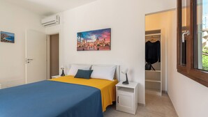 Un dormitori amb un llit, una nitzeta, una taula de nit, un armari i un quadre a la paret.