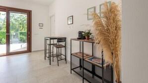 Habitació moderna amb porta de vidre corredissa que dona a una zona exterior, una taula petita amb cadires i una planta decorativa.