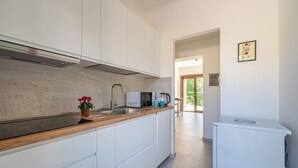 Una cuina moderna amb armaris blancs, taulell de fusta, microones integrat i un refrigerador petit.