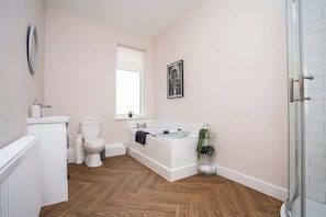 A bathroom with a white bathtub, toilet, and sink, wooden flooring, and a glass shower enclosure.
