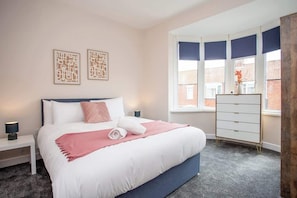 A bedroom with a bed, bedside tables, a dresser, and a window with blinds.
