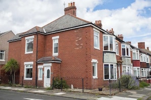 A red brick terraced house with a front door, windows, and a small garden.