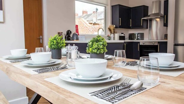 Una cocina moderna con armarios oscuros, electrodomésticos de acero inoxidable y una zona de comedor preparada para una comida.