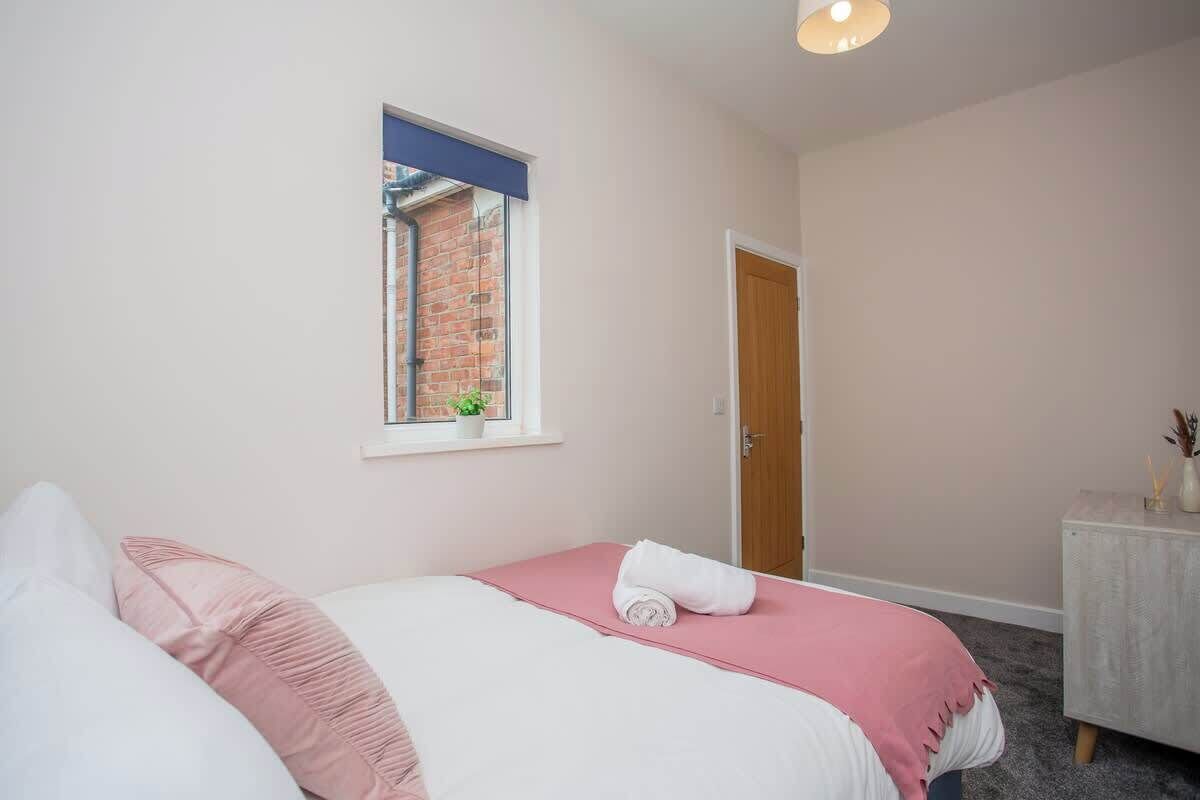 Un dormitorio con una cama, una ventana, una puerta y una mesita con una planta.