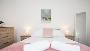 Een slaapkamer met een bed, twee nachtkastjes, een spiegel en een kunstwerk aan de muur.