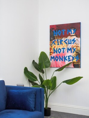A room with a blue sofa, a large potted plant, and a colorful wall art piece with text.