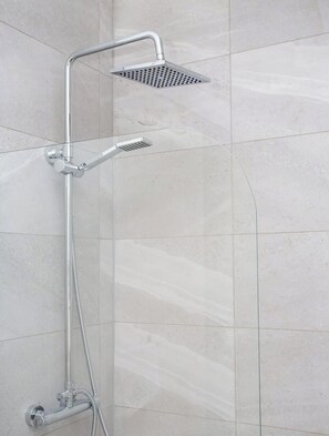 A shower with a handheld showerhead and a fixed showerhead, mounted on a wall with a tiled surface.