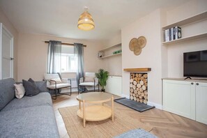 A living room with a sofa, chairs, a round table, a television, a fireplace, and bookshelves.